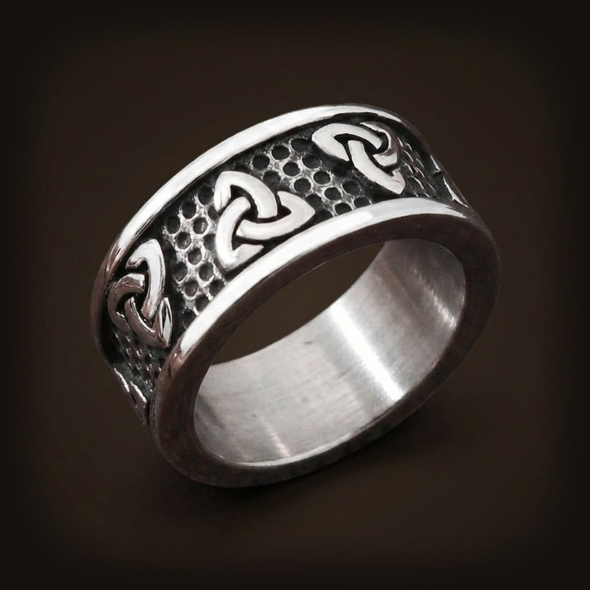 Bague viking en acier inoxydable avec symboles Triquetra polis sur fond texturé noirci.