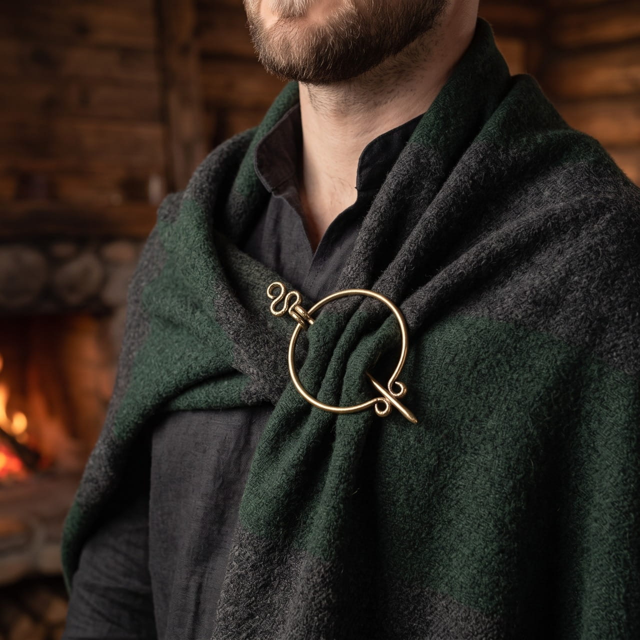 Homme portant une fibule viking pénannulaire dorée à spirales sur un châle de laine verte