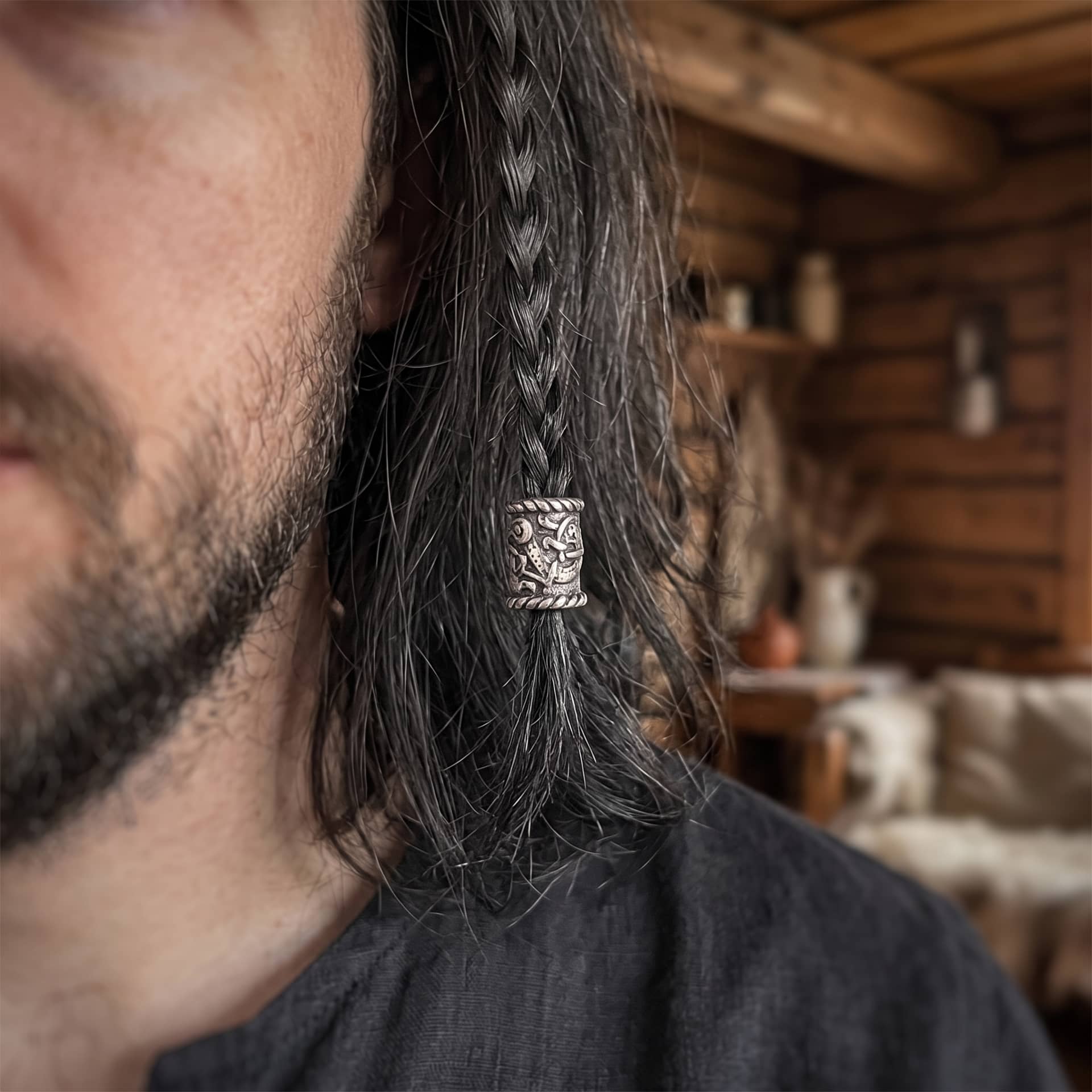 Perle viking en alliage argent vieilli, ornée d'une bête en ruban de style d'Urnes entre deux bordures torsadées, portée sur une fine tresse de cheveux