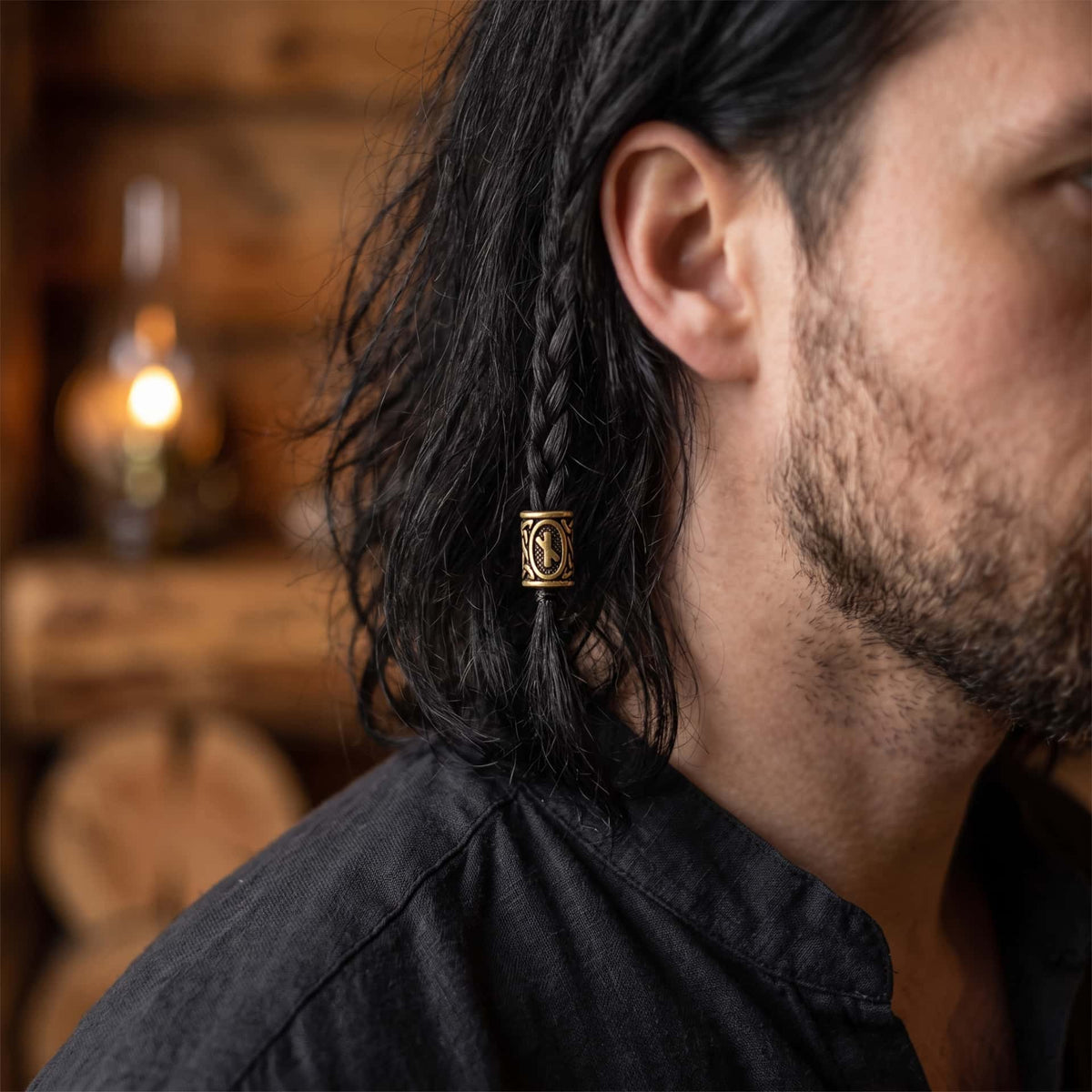 Perle viking en alliage bronze patiné, gravée de la rune Nauthiz dans un cartouche ovale, portée sur une fine tresse de cheveux