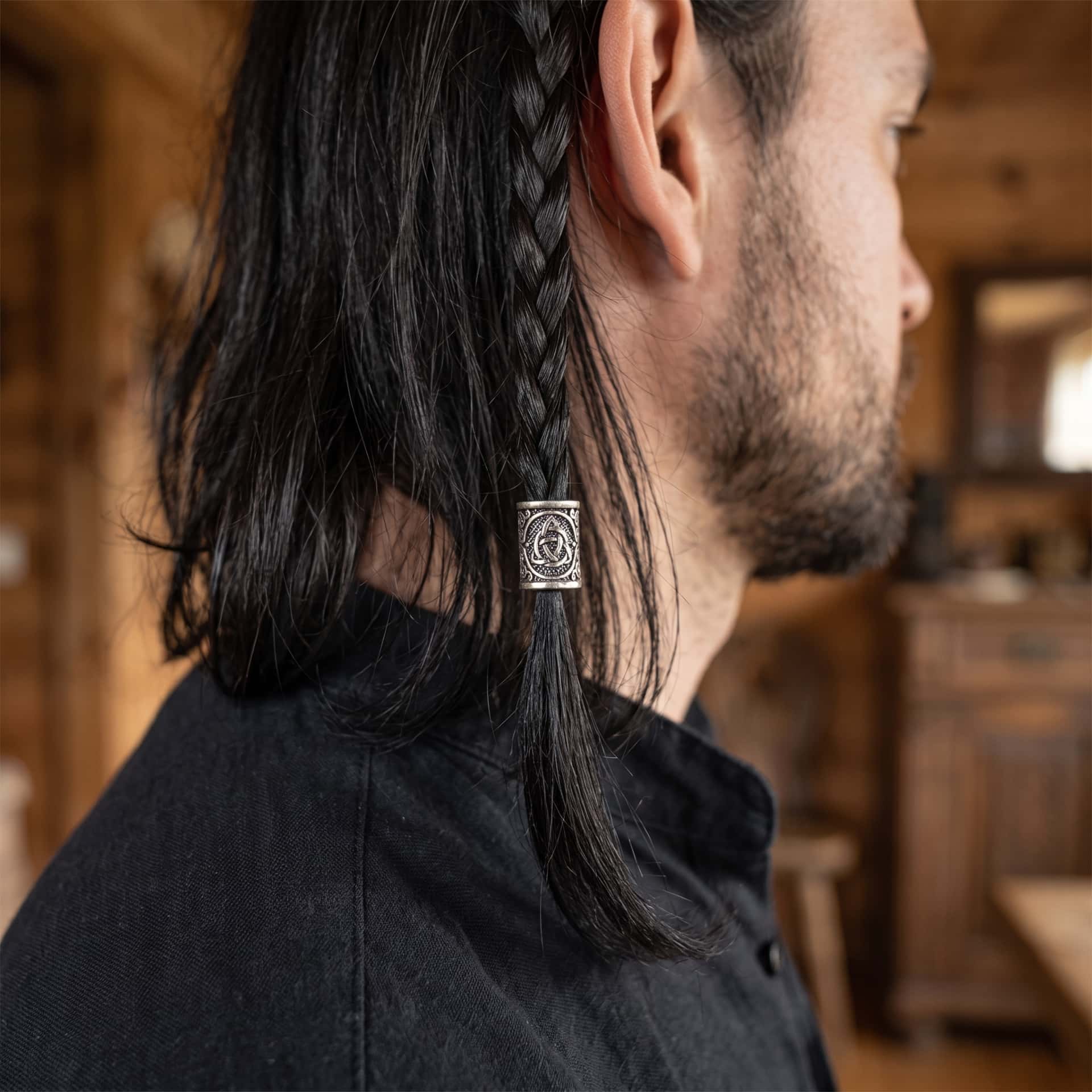 Perle viking en alliage argent vieilli, gravée d'une triquetra centrée dans un médaillon cerné de volutes, portée sur une fine tresse de cheveux