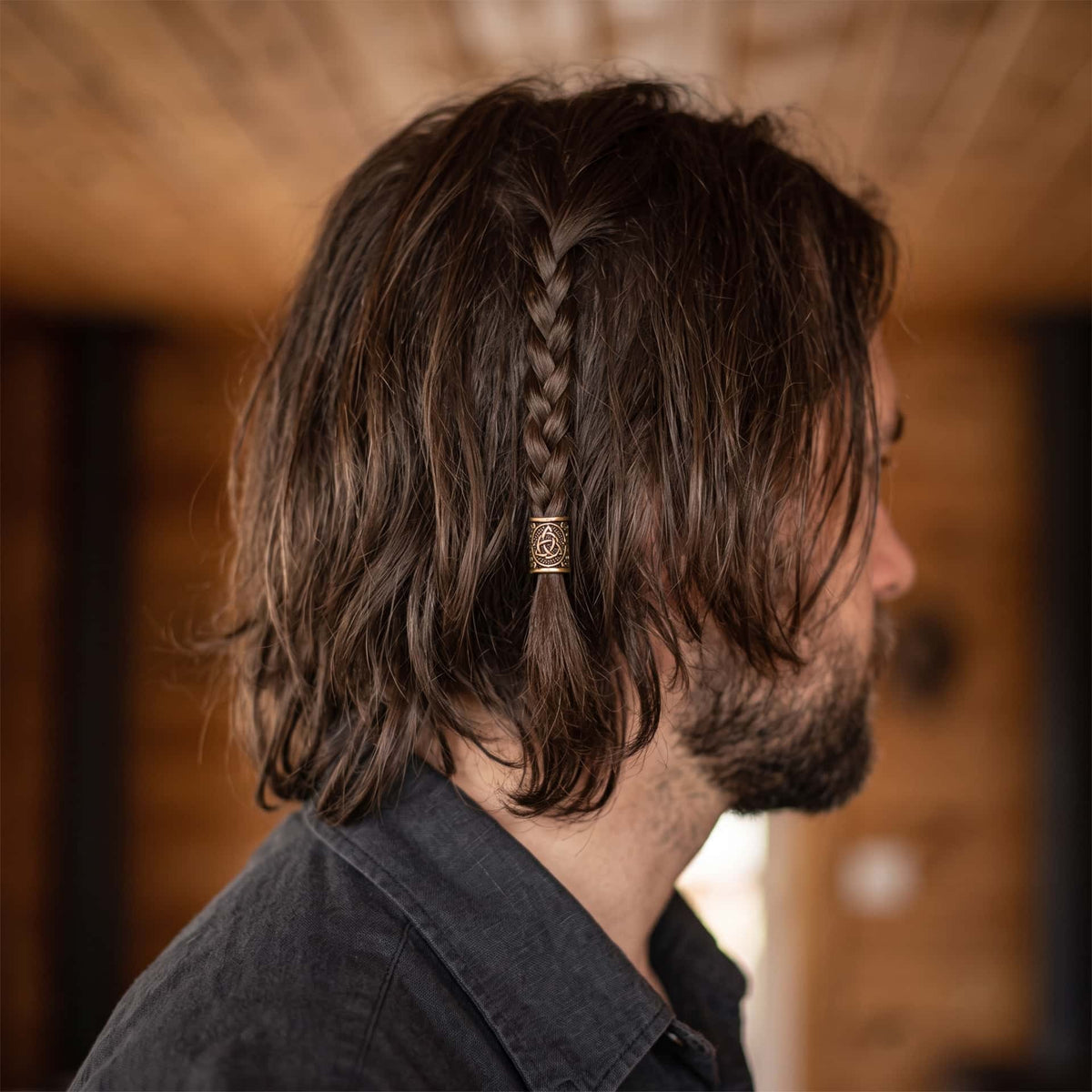 Perle viking en alliage bronze patiné, gravée d'une triquetra centrée dans un médaillon cerné de volutes, portée sur une fine tresse de cheveux