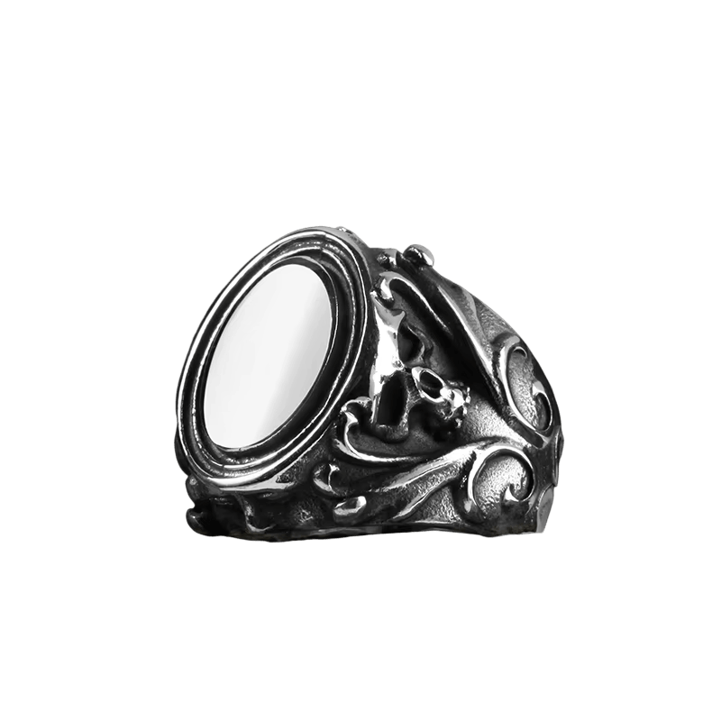 Bague en acier patiné, cabochon blanc ovale serti haut, épaules ciselées de petits crânes et de volutes