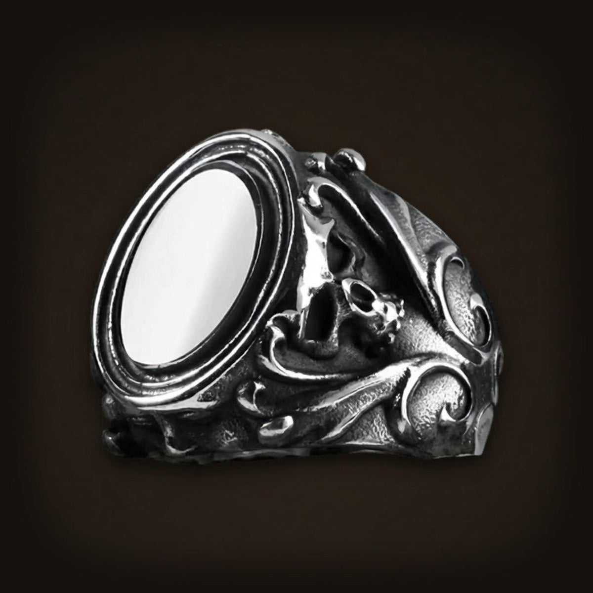 Bague en acier patiné, cabochon blanc ovale serti haut, épaules ciselées de petits crânes et de volutes