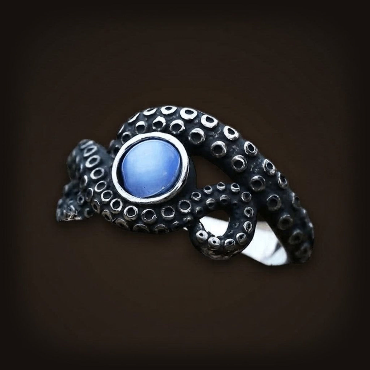 Bague en acier noirci en forme de tentacule à ventouses, enroulé sur une pierre bleue à effet œil-de-chat
