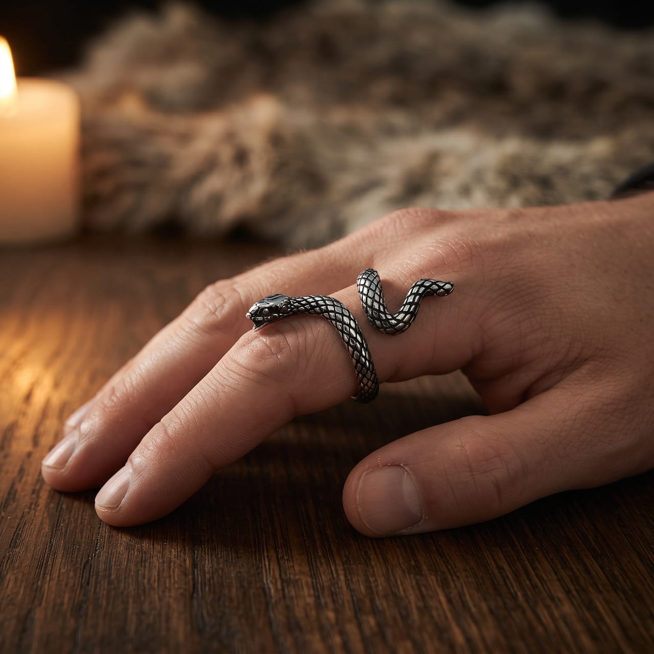 Bague serpent en acier aux écailles ciselées enroulée sur l'index d'une main d'homme, tête vers l'ongle, fourrure et bougie en fond