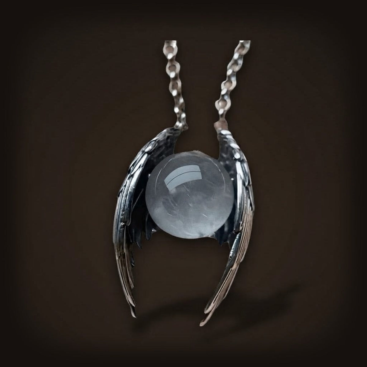 Collier Ailes Noires et Sphère de Verre en alliage de zinc : deux ailes noires aux reflets argentés enserrant une sphère de verre transparente, sur sa chaîne