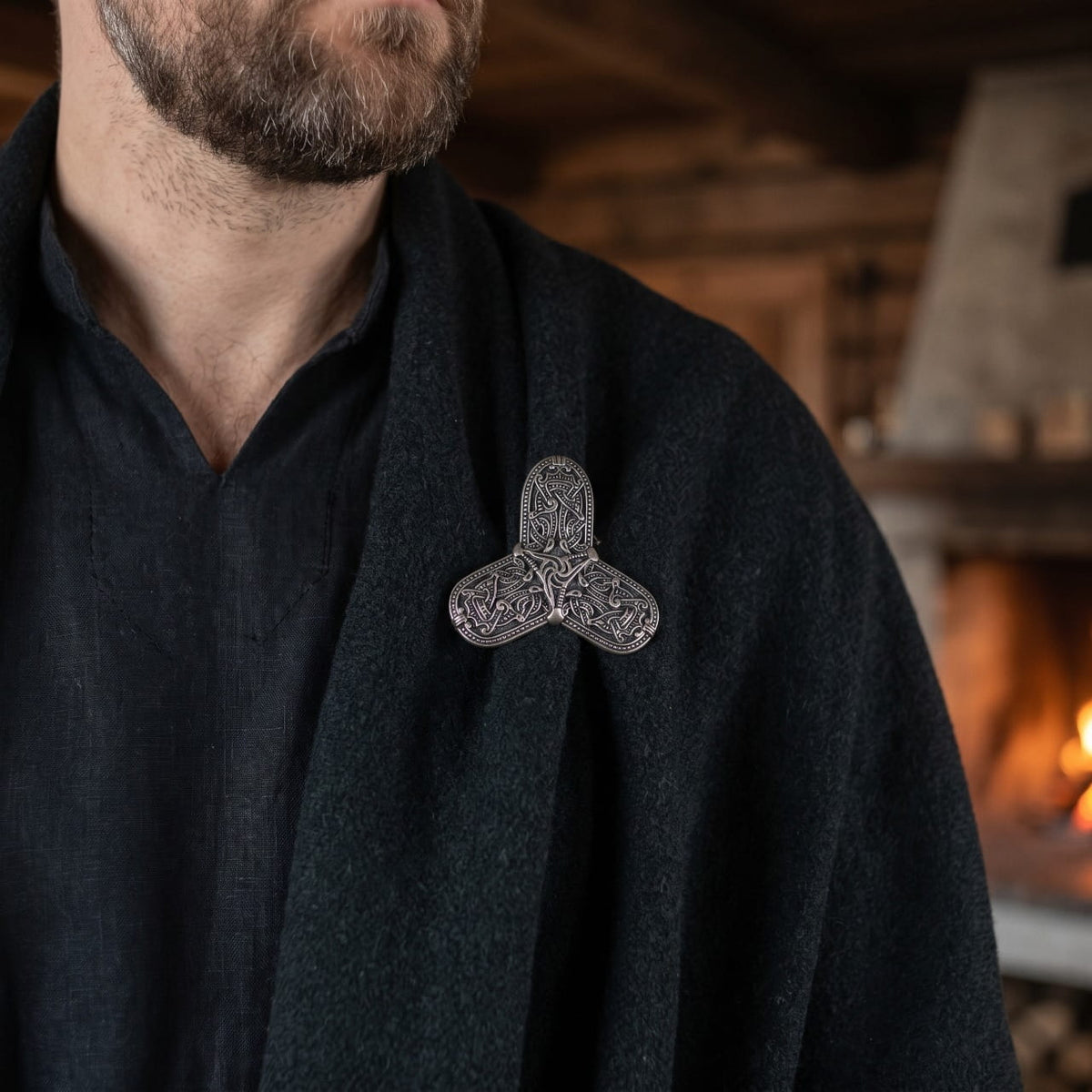 Homme portant une fibule viking trilobée en argent vieilli sur une cape de laine sombre