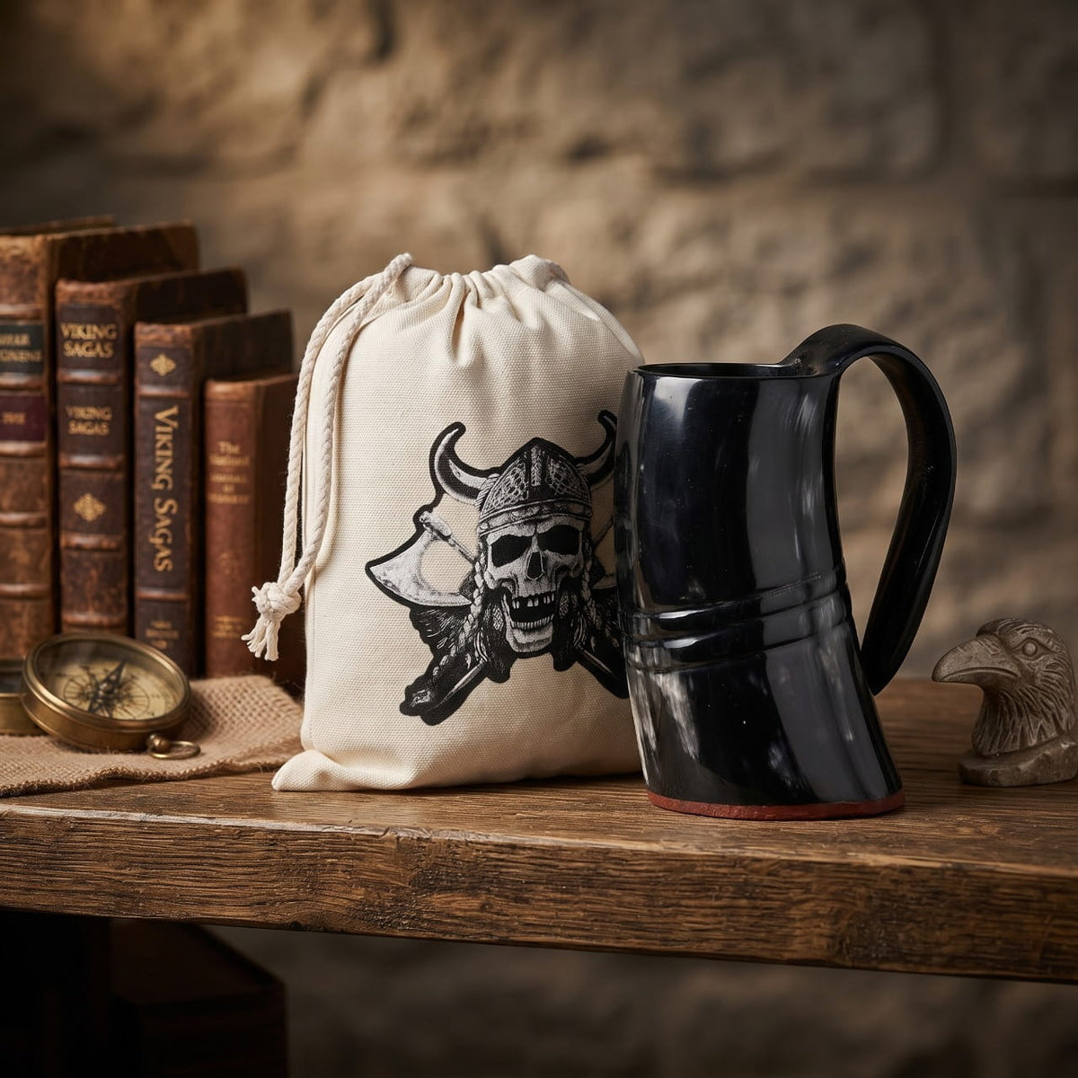 Mug viking en corne de buffle sombre, à côté de son sac en toile imprimé, sur une table de bois devant un mur de pierre