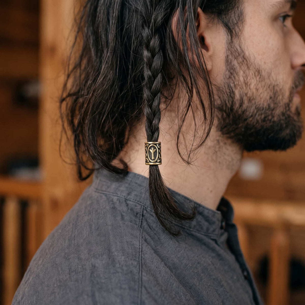 Perle viking en alliage bronze patiné, gravée de la rune Algiz dans un cartouche ovale, portée sur une fine tresse de cheveux