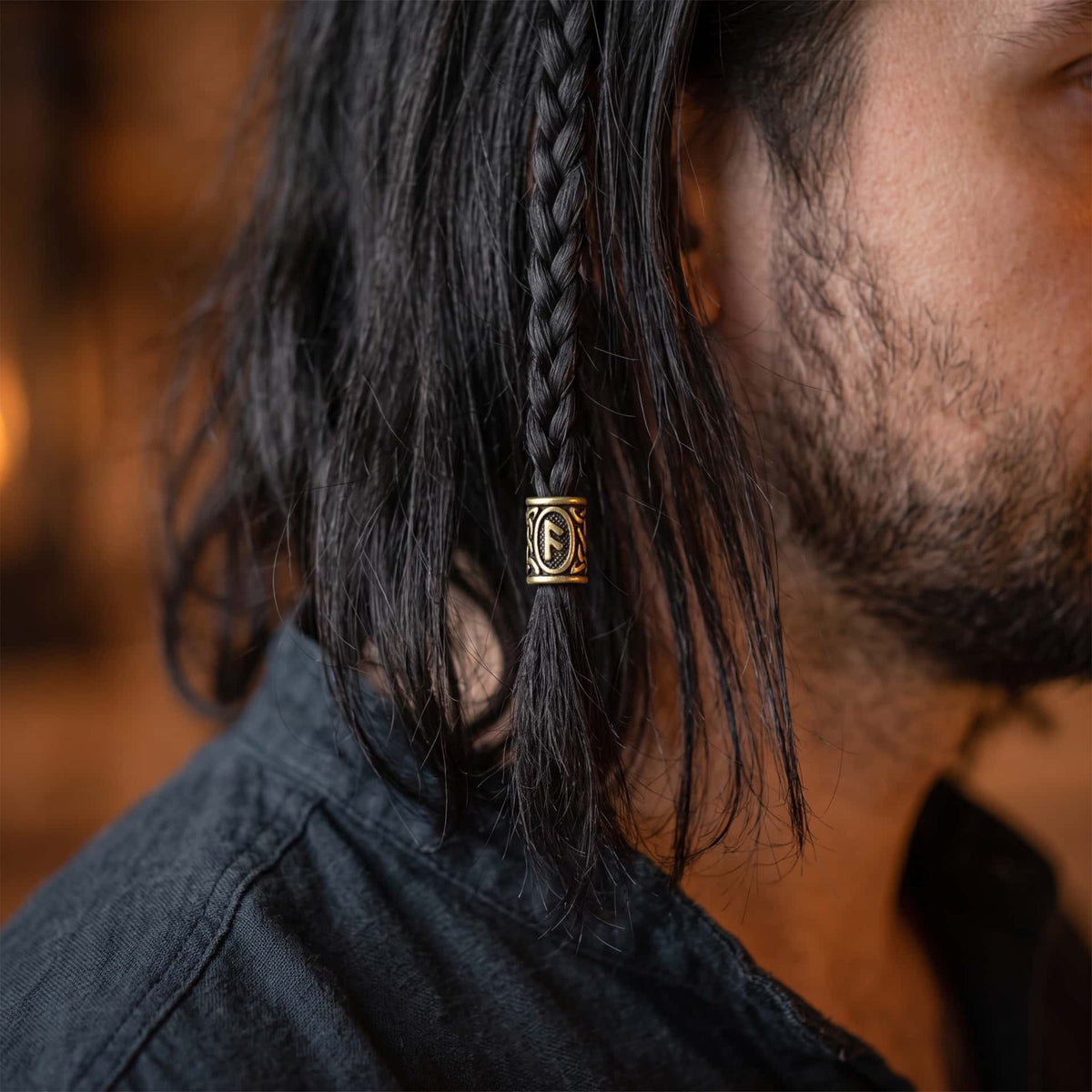 Perle viking en alliage bronze patiné, gravée de la rune Ansuz dans un cartouche ovale, portée sur une fine tresse de cheveux