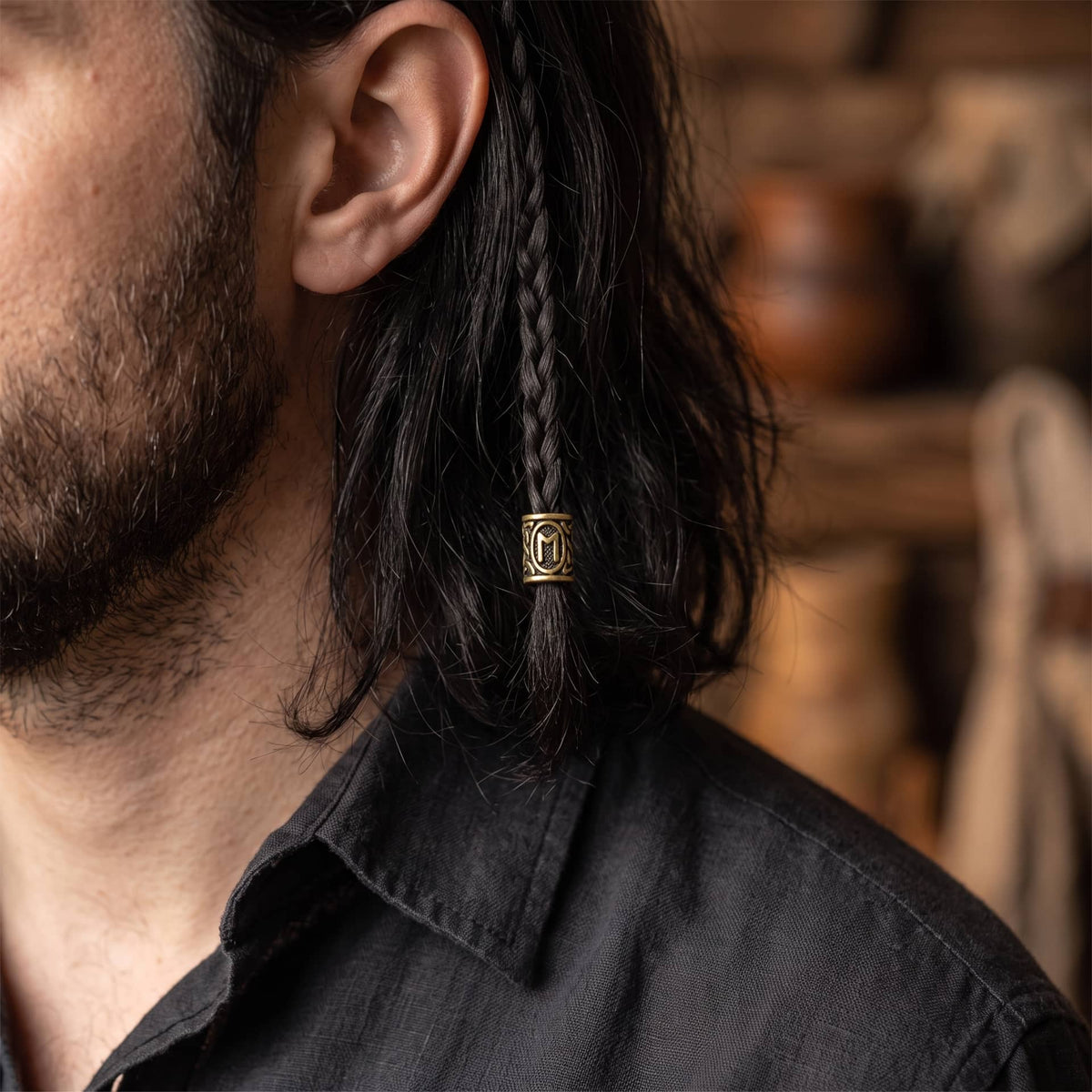 Perle viking en alliage bronze patiné, gravée de la rune Ehwaz dans un cartouche ovale, portée sur une fine tresse de cheveux