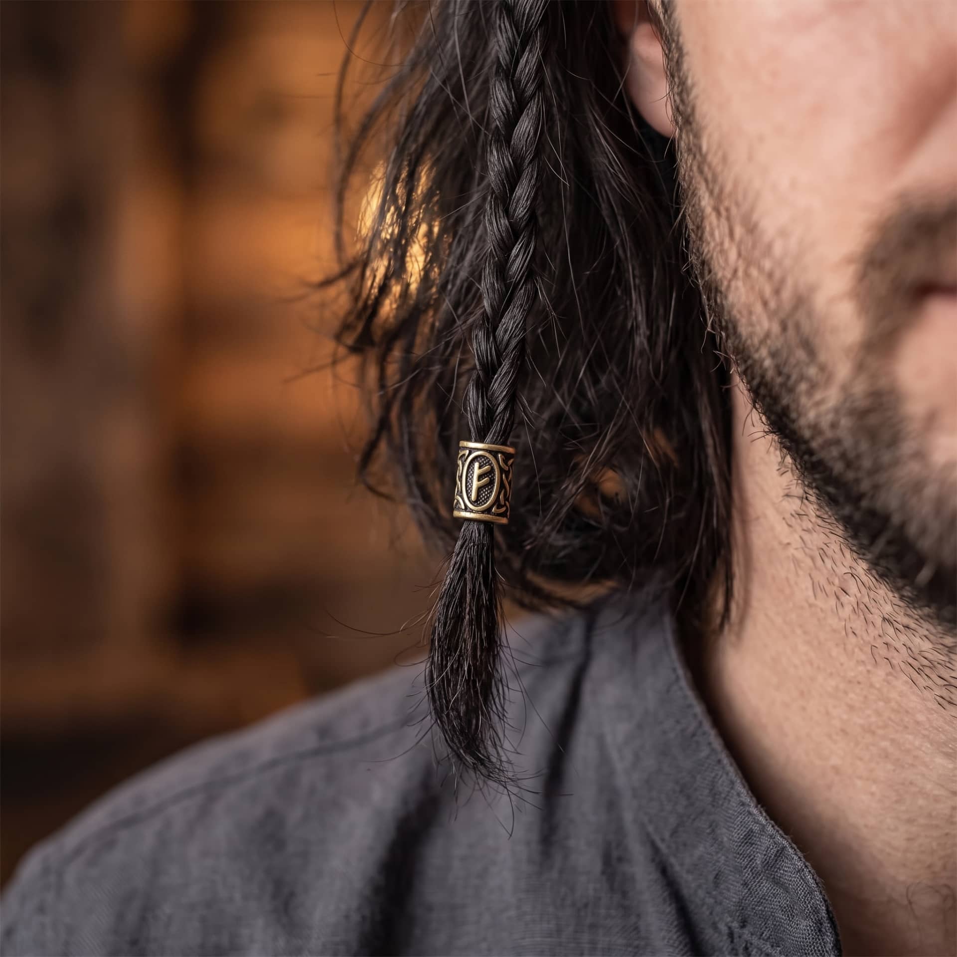 Perle viking en alliage bronze patiné, gravée de la rune Fehu dans un cartouche ovale, portée sur une fine tresse de cheveux