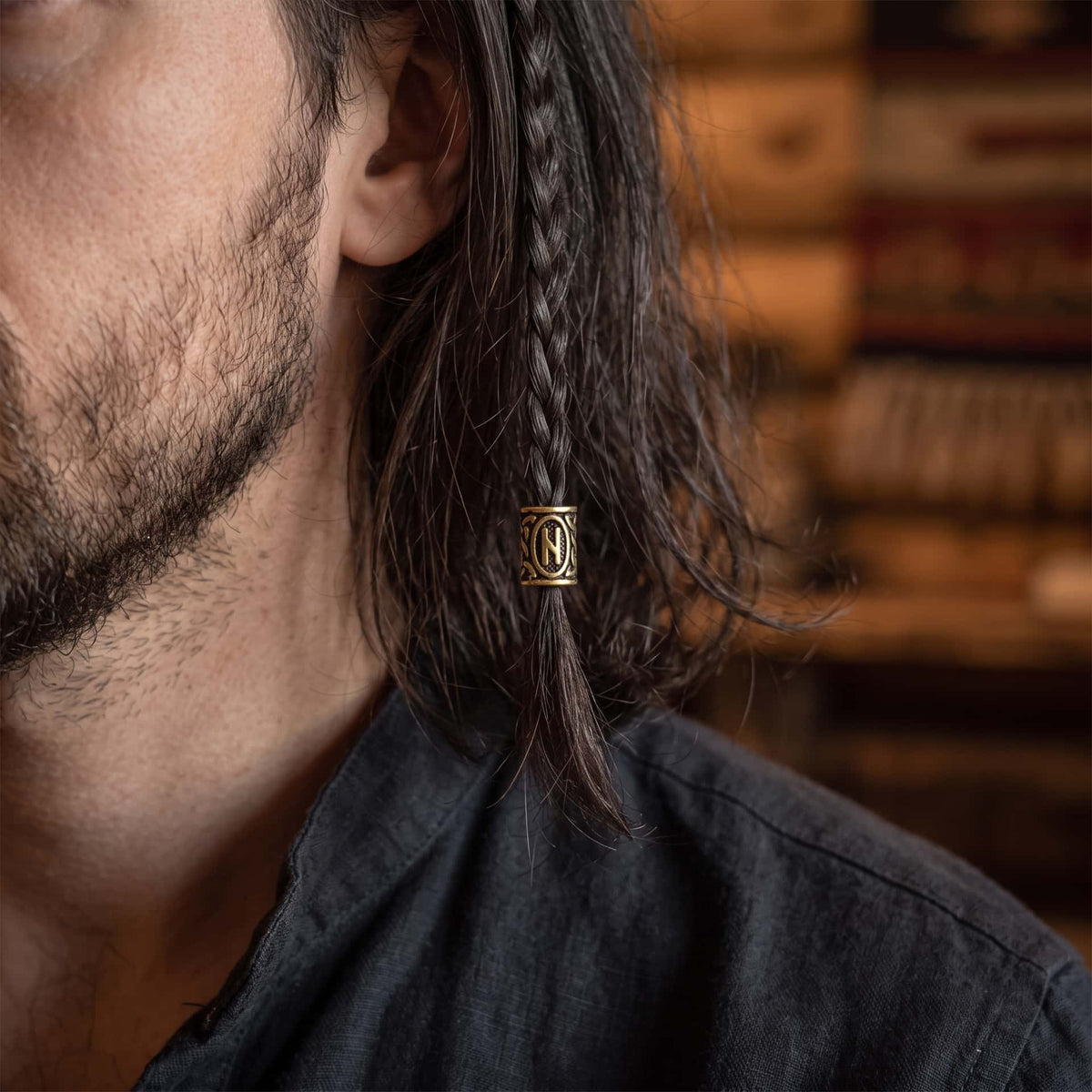 Perle viking en alliage bronze patiné, gravée de la rune Hagalaz dans un cartouche ovale, portée sur une fine tresse de cheveux