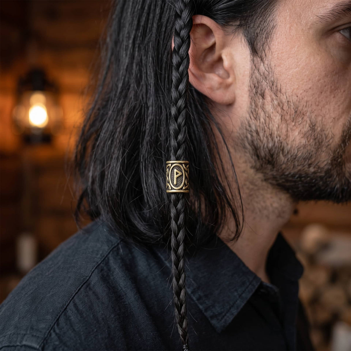 Perle viking en alliage bronze patiné, gravée de la rune Wunjo dans un cartouche ovale, portée sur une fine tresse de cheveux